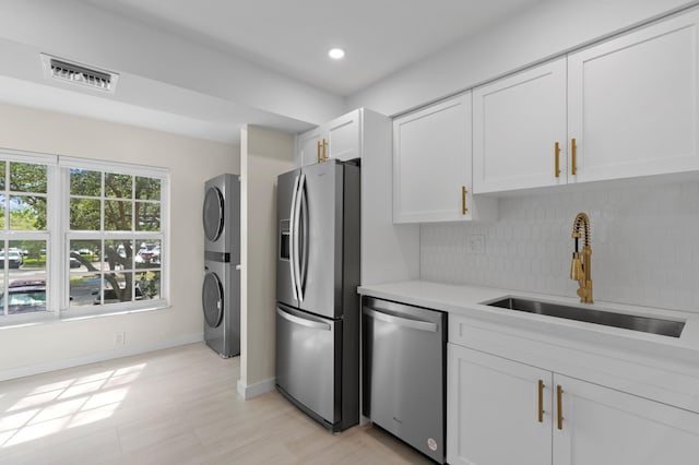 kitchen featuring white cabinetry, sink, stainless steel appliances, stacked washer / dryer, and decorative backsplash