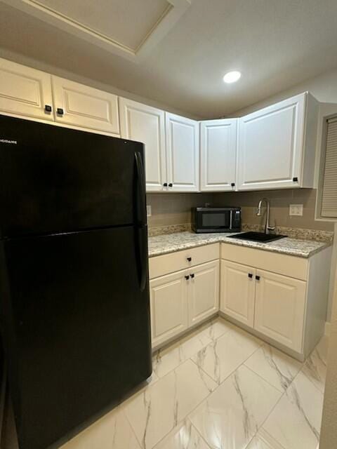 kitchen with white cabinetry, black refrigerator, sink, and light stone counters