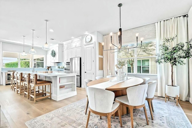 dining area with a notable chandelier, wine cooler, and light hardwood / wood-style flooring