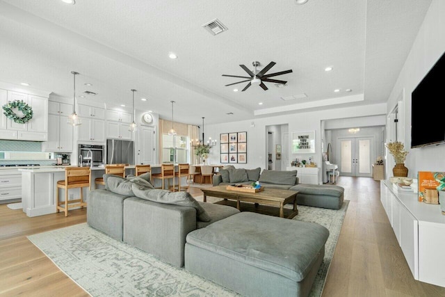 living room featuring light wood-type flooring, a textured ceiling, a tray ceiling, and ceiling fan