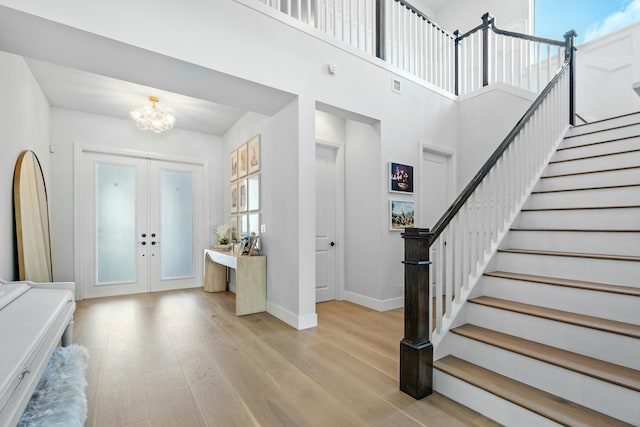 entrance foyer with a chandelier, light wood-type flooring, a towering ceiling, and french doors