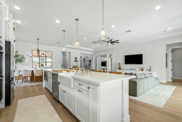 kitchen featuring sink, pendant lighting, a kitchen island with sink, white cabinets, and ceiling fan with notable chandelier