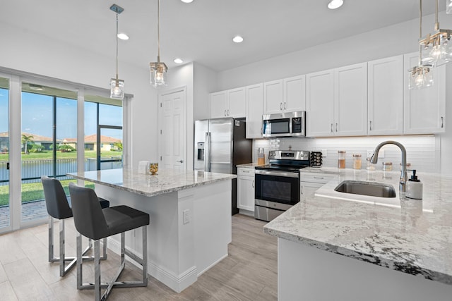 kitchen with sink, a center island, stainless steel appliances, white cabinets, and a water view