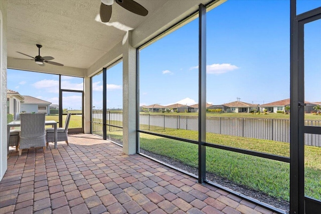 unfurnished sunroom featuring ceiling fan and a water view