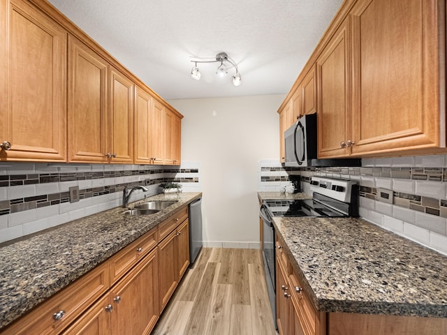 kitchen with appliances with stainless steel finishes, brown cabinets, a sink, and light wood finished floors