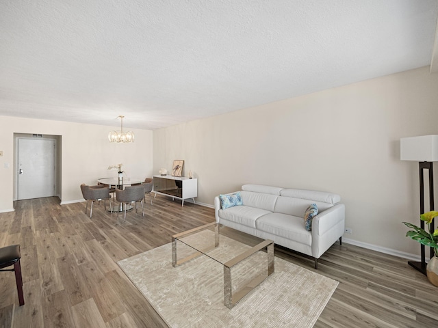 living area with baseboards, a textured ceiling, wood finished floors, and an inviting chandelier