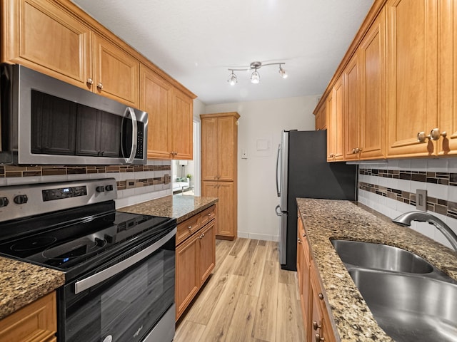 kitchen featuring dark stone counters, a sink, stainless steel appliances, light wood-style floors, and backsplash