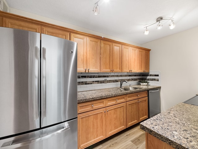 kitchen with light wood finished floors, backsplash, appliances with stainless steel finishes, stone countertops, and a sink