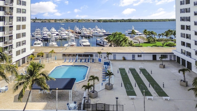 community pool with a patio area, fence, and a water view