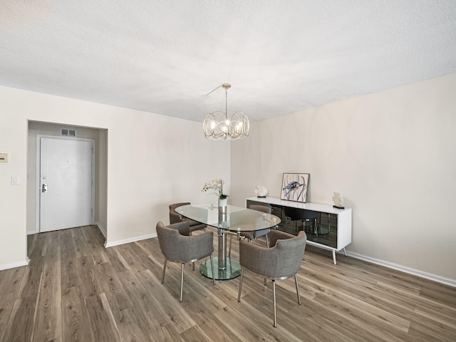 dining room featuring baseboards, visible vents, wood finished floors, a textured ceiling, and a chandelier