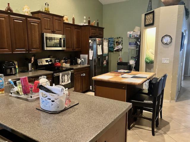 kitchen with a center island, light tile patterned flooring, dark brown cabinetry, and appliances with stainless steel finishes