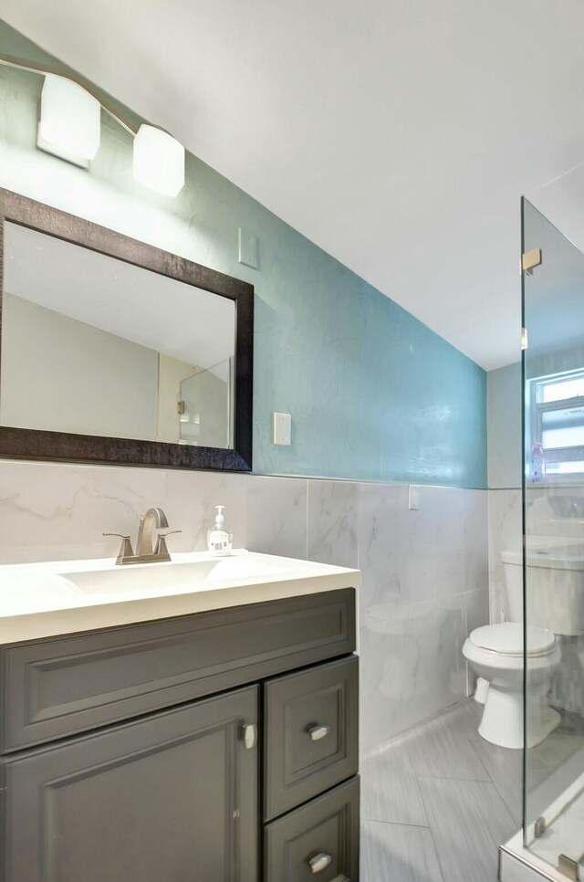 bathroom with vanity, toilet, tile walls, and a shower with shower door