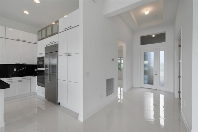 kitchen featuring white cabinetry, backsplash, double oven, built in refrigerator, and a tray ceiling