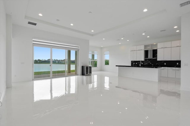 kitchen with white cabinets, a water view, wall chimney range hood, decorative backsplash, and light tile patterned floors