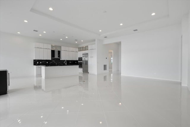 kitchen with wall chimney exhaust hood, a raised ceiling, built in fridge, light tile patterned flooring, and white cabinets