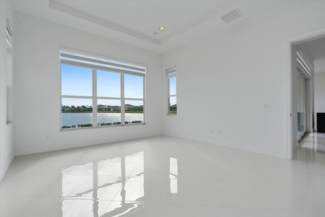 empty room with a raised ceiling, a water view, and light tile patterned floors