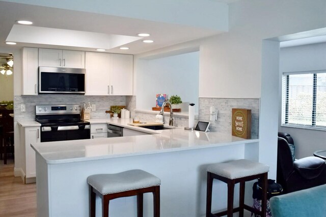 kitchen featuring backsplash, white cabinetry, a sink, dishwasher, and a peninsula