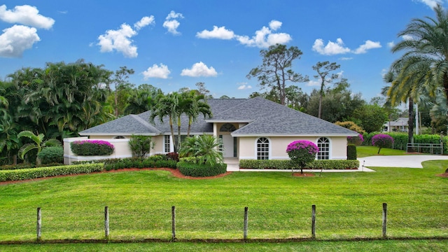 ranch-style house with a front yard, roof with shingles, fence, and stucco siding