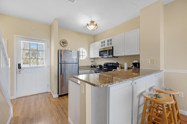 kitchen featuring stainless steel appliances, a peninsula, a healthy amount of sunlight, light stone countertops, and glass insert cabinets