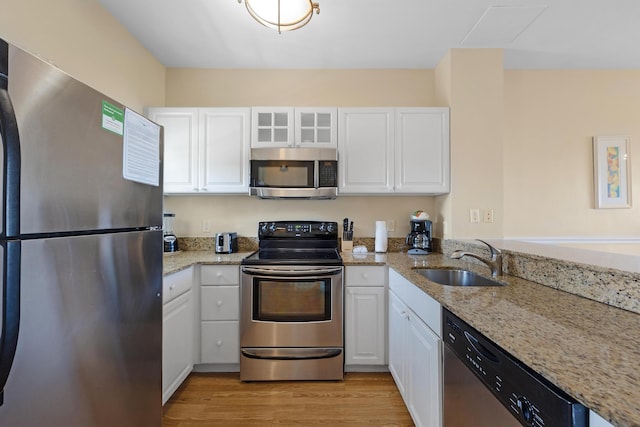 kitchen featuring light stone counters, a sink, light wood-style floors, white cabinets, and appliances with stainless steel finishes