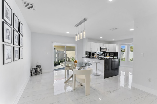 kitchen with stainless steel appliances, a kitchen breakfast bar, decorative light fixtures, decorative backsplash, and white cabinets