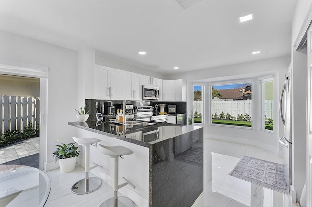 kitchen with white cabinetry, stainless steel appliances, backsplash, kitchen peninsula, and dark stone countertops