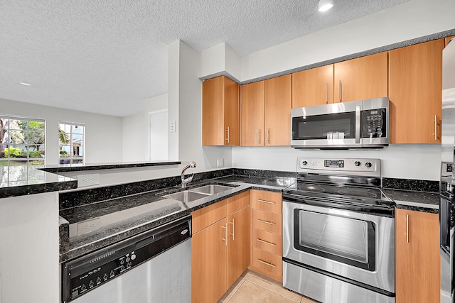 kitchen with a textured ceiling, dark stone countertops, sink, and stainless steel appliances