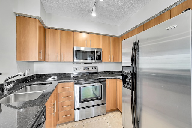 kitchen featuring appliances with stainless steel finishes, track lighting, a textured ceiling, sink, and light tile patterned flooring