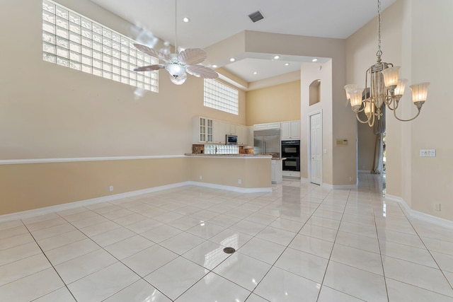 interior space with ceiling fan with notable chandelier, light tile patterned floors, and a towering ceiling