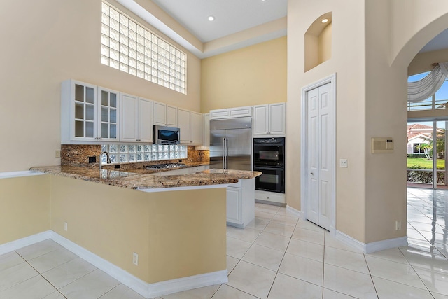 kitchen featuring kitchen peninsula, stone counters, stainless steel appliances, and a high ceiling