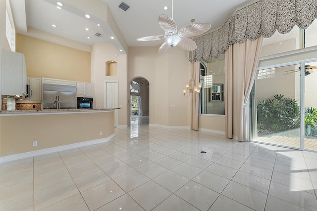 unfurnished living room featuring ceiling fan, light tile patterned floors, and a high ceiling