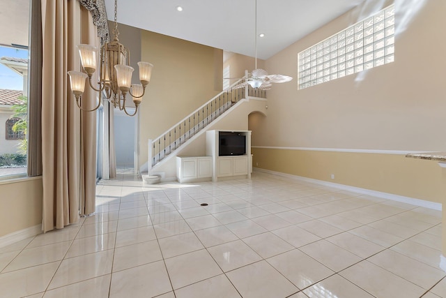 unfurnished living room featuring a towering ceiling, light tile patterned floors, and ceiling fan with notable chandelier