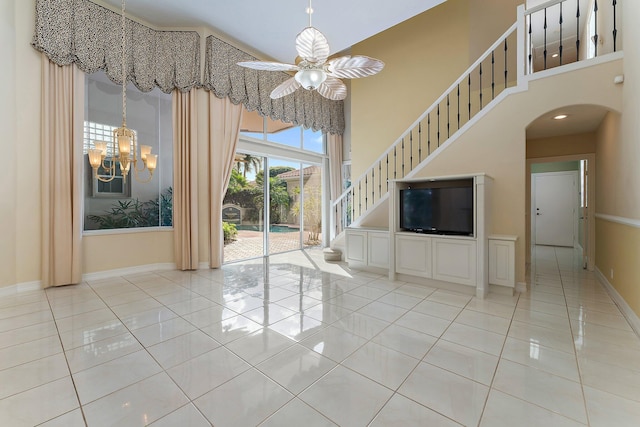 unfurnished living room featuring ceiling fan with notable chandelier, light tile patterned floors, and a towering ceiling