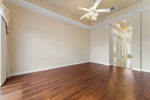 empty room with a raised ceiling, ceiling fan, and dark hardwood / wood-style floors