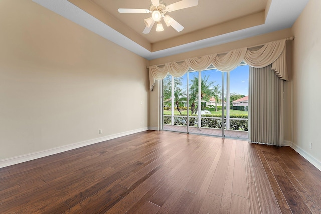 empty room featuring a raised ceiling, ceiling fan, and dark hardwood / wood-style floors