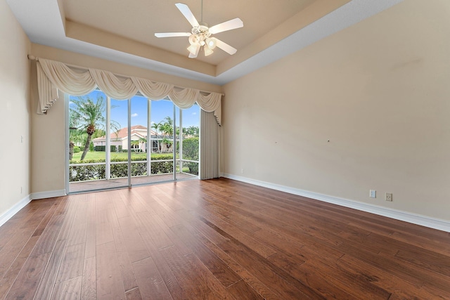 empty room with a raised ceiling, ceiling fan, and wood-type flooring