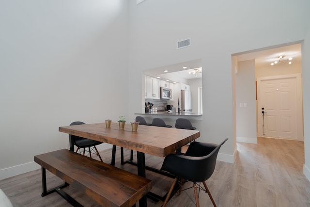 dining area with a high ceiling, light hardwood / wood-style flooring, and a notable chandelier