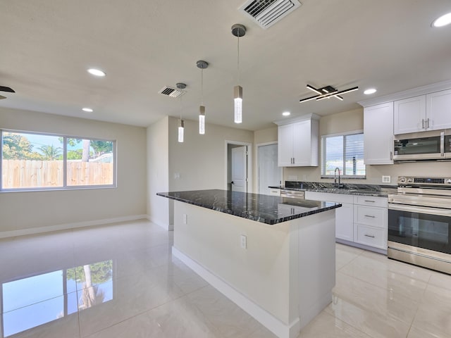 kitchen with dark stone countertops, appliances with stainless steel finishes, a center island, sink, and white cabinetry