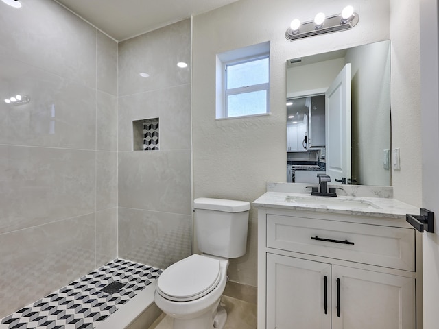 bathroom with a tile shower, vanity, and toilet