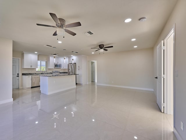 kitchen featuring dark stone countertops, appliances with stainless steel finishes, a kitchen island, white cabinets, and decorative light fixtures