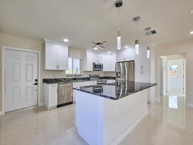 kitchen featuring hanging light fixtures, a center island, stainless steel appliances, white cabinets, and dark stone countertops