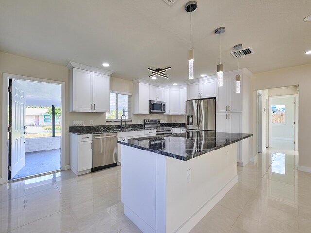 kitchen with a center island, hanging light fixtures, stainless steel appliances, white cabinets, and dark stone countertops