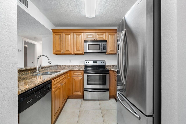 kitchen featuring a textured ceiling, stainless steel appliances, sink, light tile patterned floors, and stone countertops