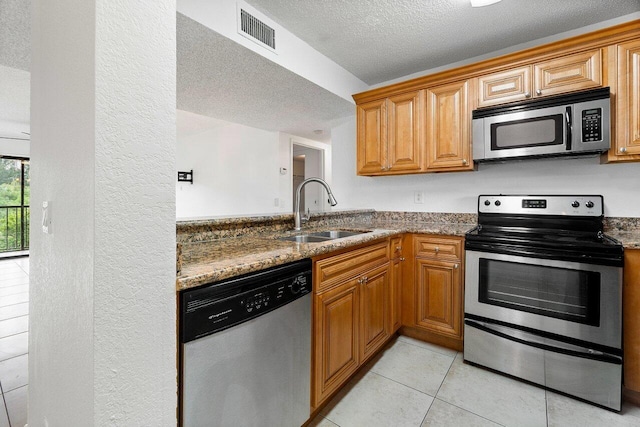 kitchen featuring sink, stainless steel appliances, dark stone countertops, a textured ceiling, and light tile patterned flooring