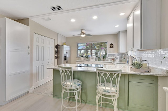 kitchen featuring a breakfast bar, kitchen peninsula, stainless steel refrigerator with ice dispenser, light stone counters, and white cabinetry