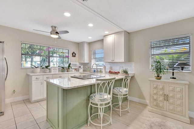 kitchen featuring light stone countertops, backsplash, a kitchen bar, black electric stovetop, and white cabinets