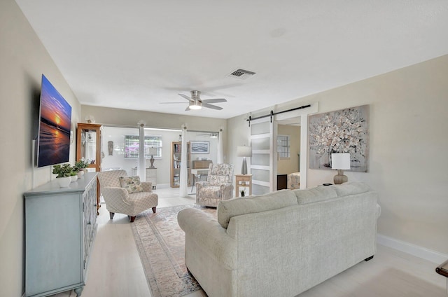 living room with light wood-type flooring, a barn door, and ceiling fan