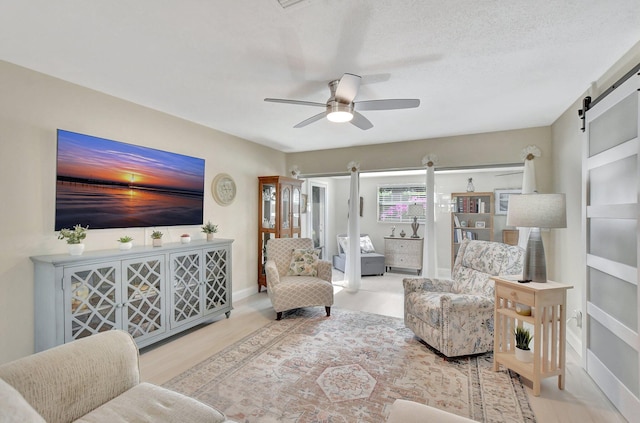 living room featuring a barn door, ceiling fan, wood-type flooring, and a textured ceiling