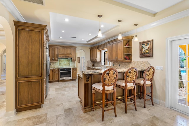 kitchen with hanging light fixtures, oven, light stone counters, kitchen peninsula, and a raised ceiling