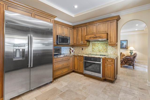 kitchen featuring premium range hood, light stone counters, ornamental molding, appliances with stainless steel finishes, and decorative backsplash